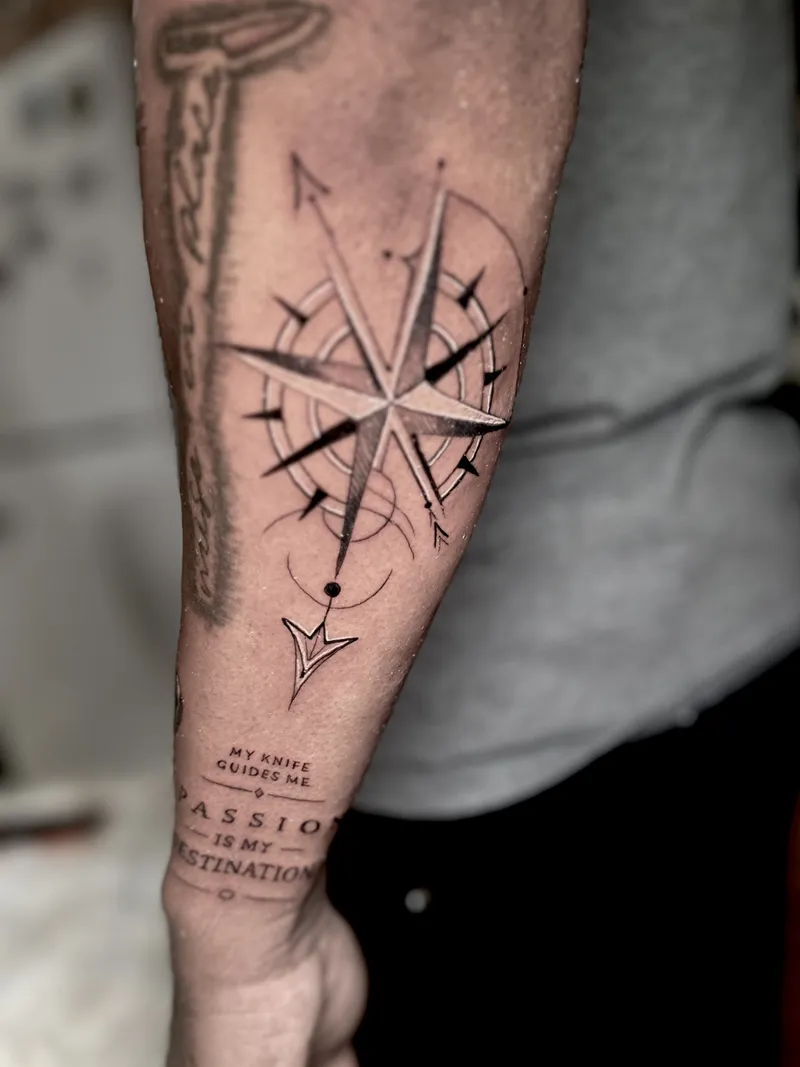 Black and grey compass rose with fine line text on the forearm