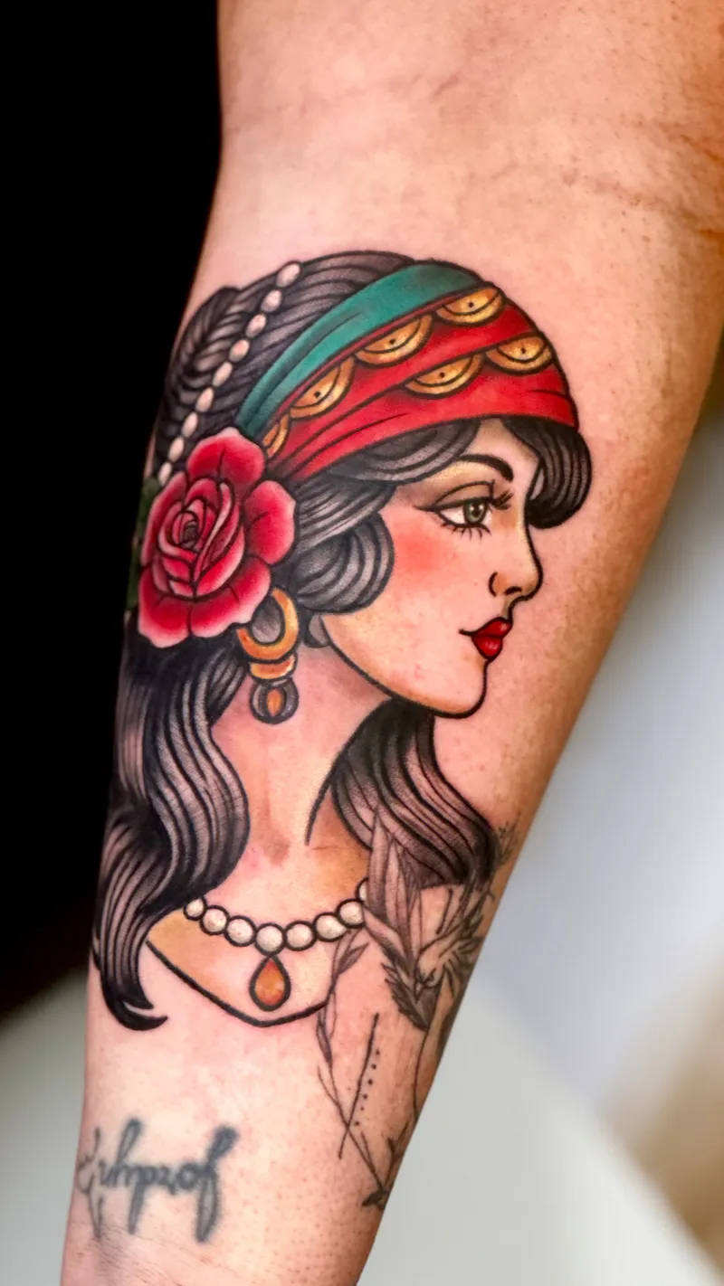 Neo-traditional gypsy woman tattoo with a red rose and headscarf on the forearm