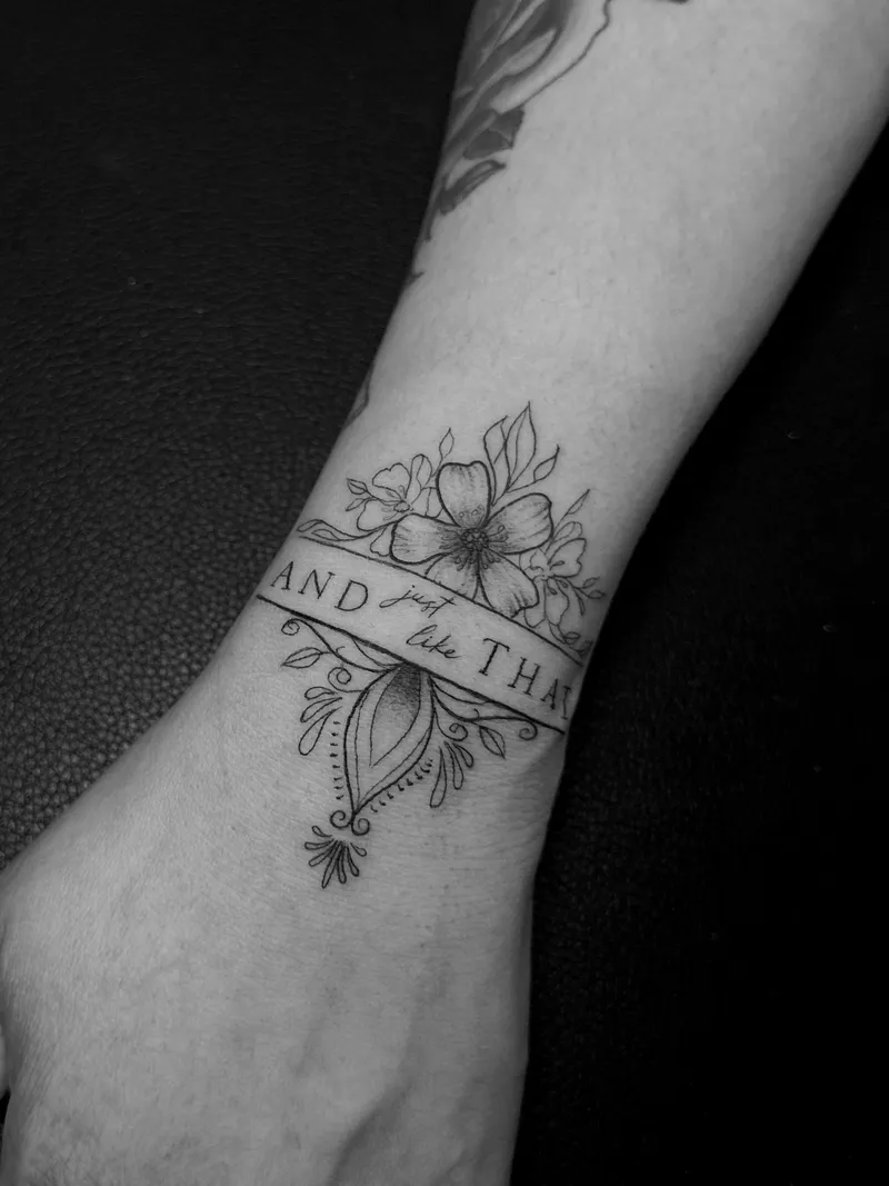 Fine line blossoms over a banner on the inner wrist
