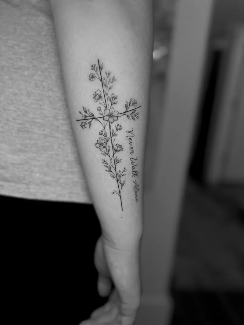 Fine line cross of wildflowers with script on the back of the arm